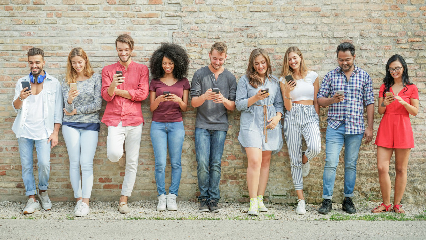 Une rangée de jeunes adossés à un mur, le mobile en main. Qui détient l’abonnement prepaid (prépayé) le moins cher ?